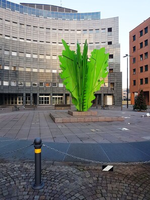Stroll through the vibrant urban plaza, surrounded by a striking green sculpture and a modern commercial building with a grid-like facade.