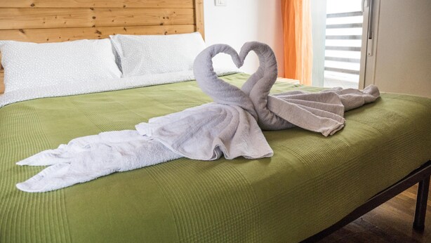 A bed with a green bedspread and two towels arranged in a swan shape. - Casa Bella Skyline (Bologna)