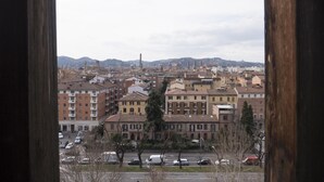 A view of a cityscape through a window, featuring a mix of residential and commercial buildings, a prominent tower, and a hilly background. - Casa Bella Skyline (Bologna)