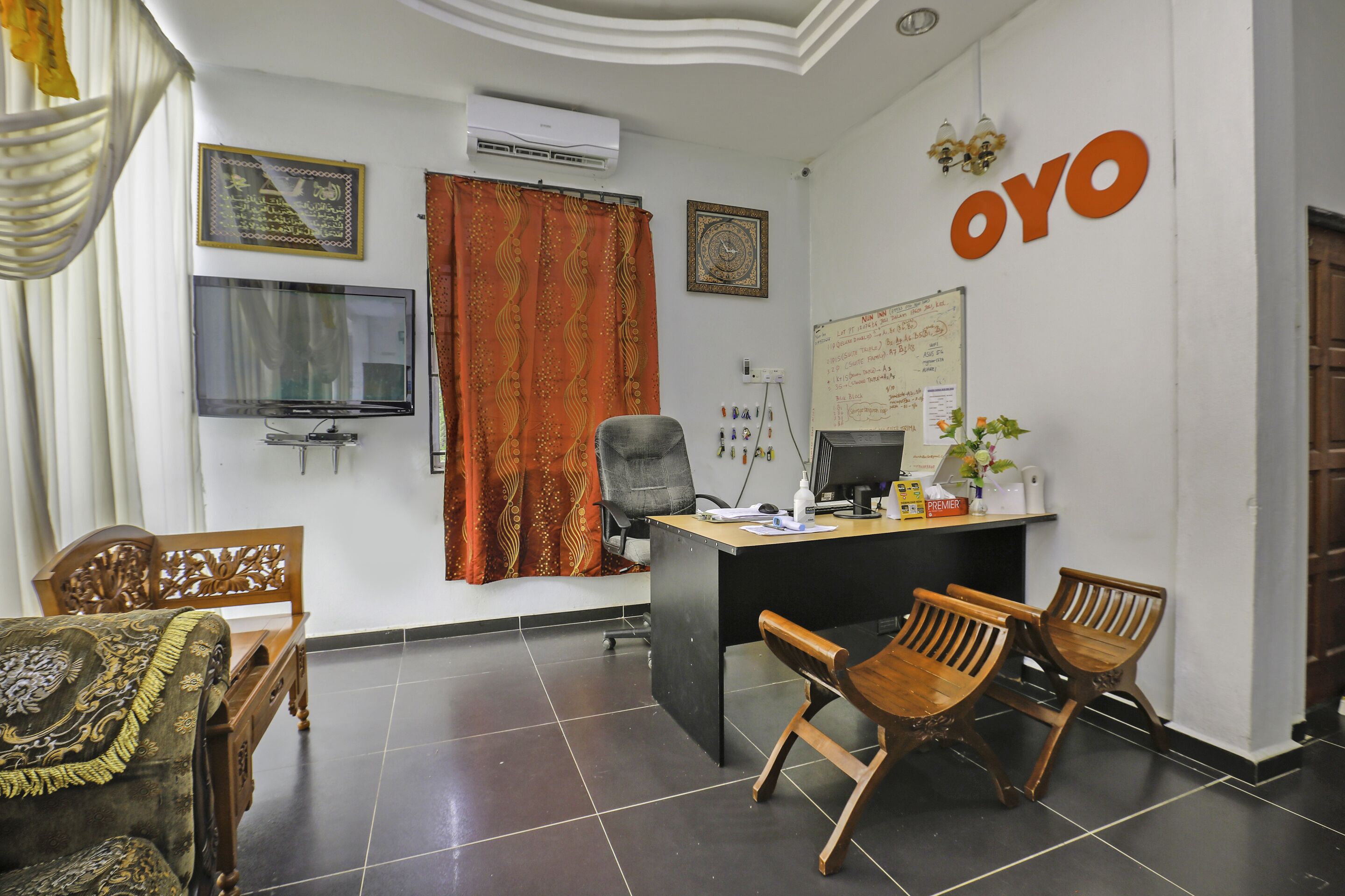 A hotel reception area with a desk, chairs, a television, and a wall-mounted air conditioner.