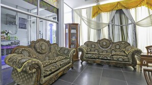 A room with two ornate sofas, a wooden cabinet, and a large window with draped curtains.