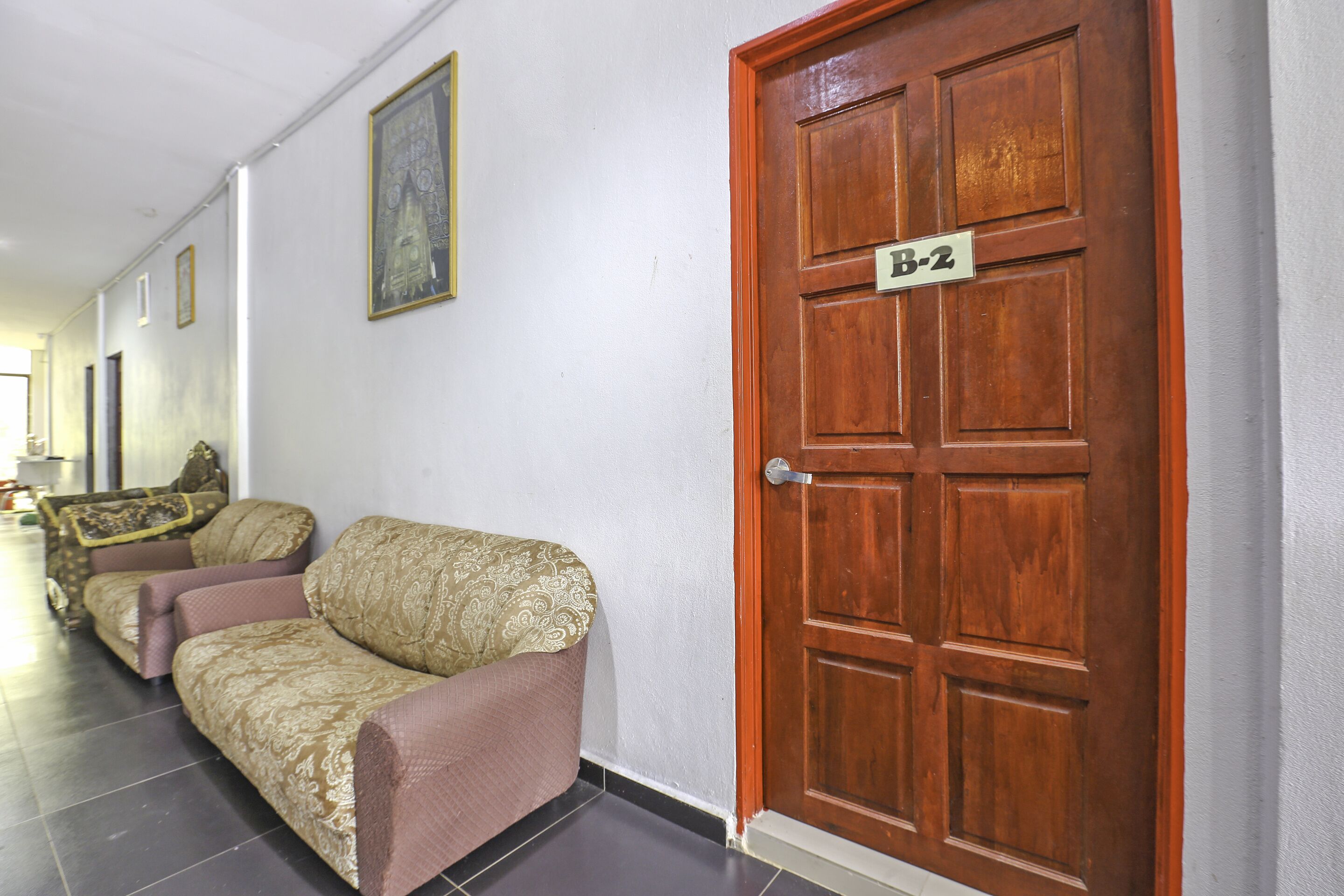 A hallway with a wooden door labeled "B-2" and a sofa with patterned upholstery.