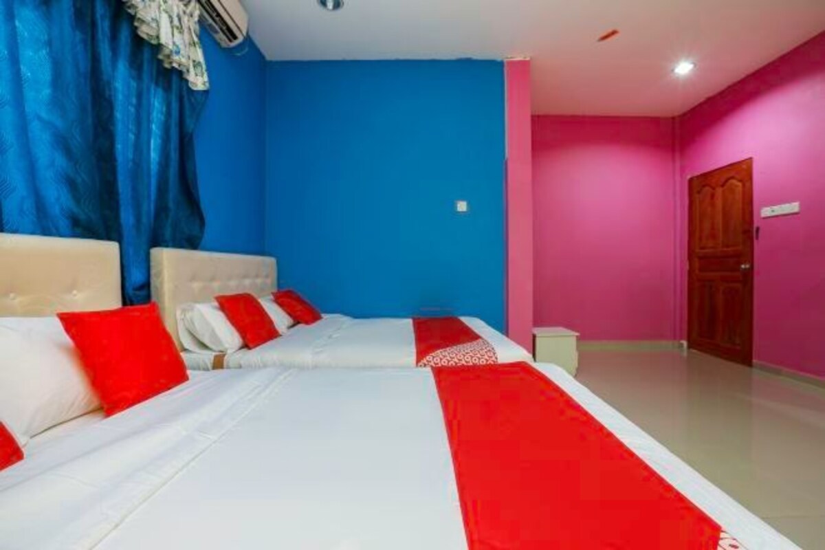 A hotel room with two beds, each with red and white bedding, a blue wall, and a pink wall.