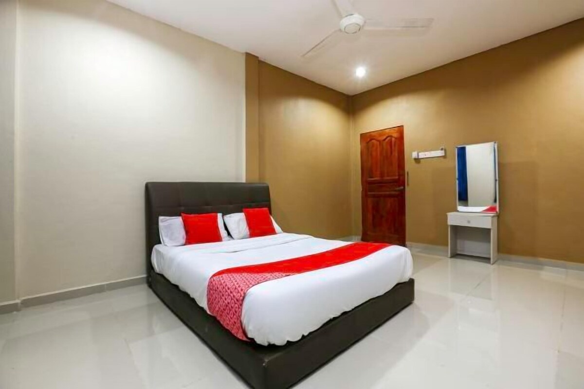 A neatly arranged hotel room with a bed, a vanity with a mirror, and a ceiling fan.
