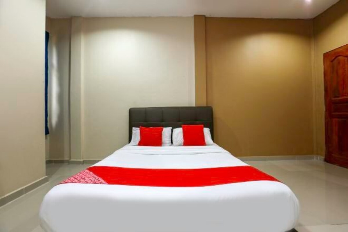 A neatly made bed with a white and red bedspread, a dark headboard, and a red accent pillow.