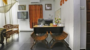 A room with a desk, two wooden chairs, a television, a whiteboard, and a large orange sign on the wall.
