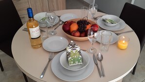 A round dining table set with plates, cutlery, a bottle of wine, a fruit bowl, a candle, and a glass of water. - Porto Paolo side sea view ( Condominium ) (St. Paul's Bay)