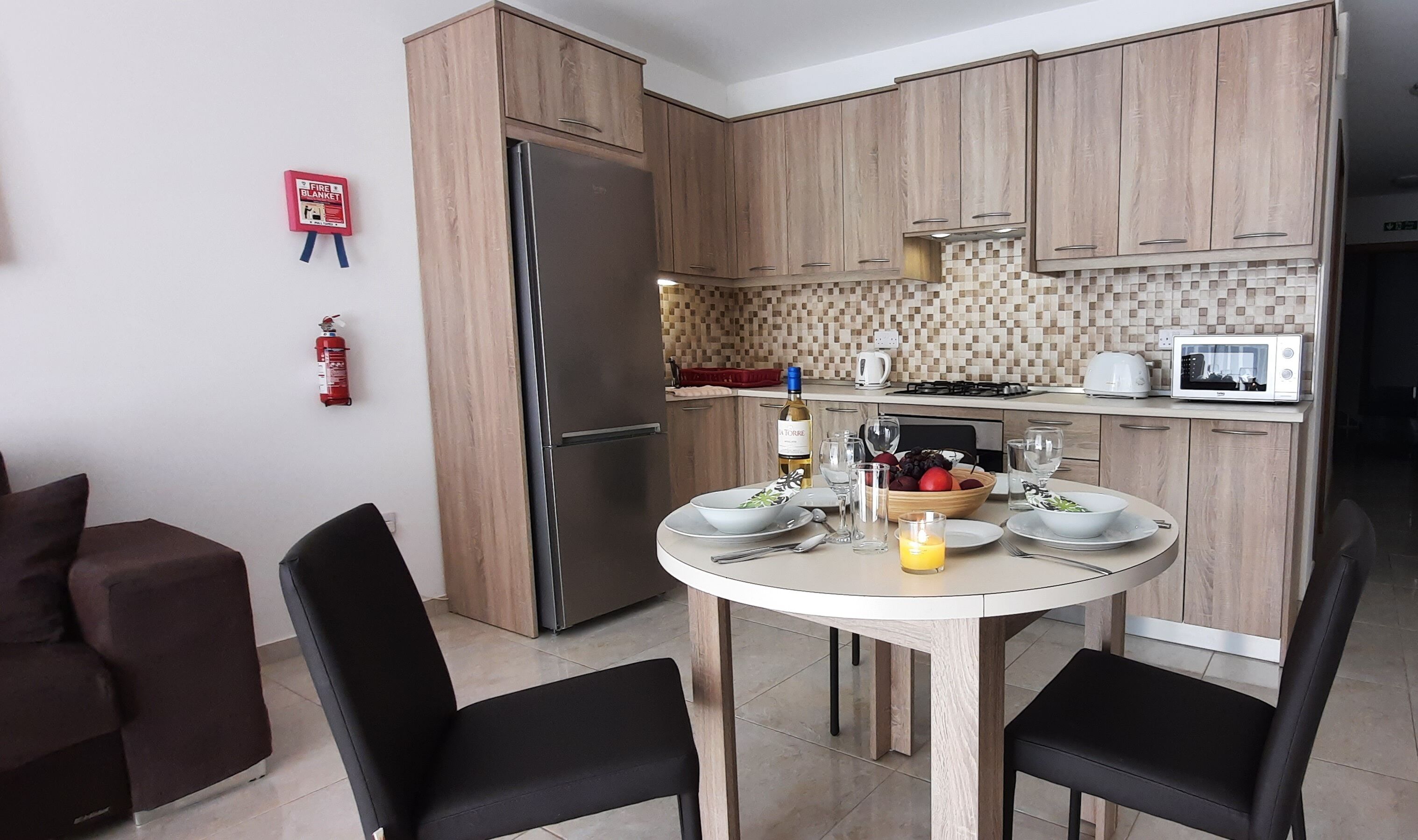 Une cuisine moderne avec des meubles en bois, un réfrigérateur en acier inoxydable et une table à manger pour quatre personnes.