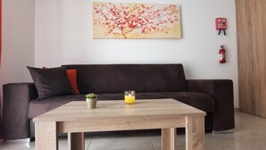 A modern living room with a dark brown sofa, a wooden coffee table, a small potted plant, a lit candle, and a fire extinguisher on the wall. - Porto Paolo side sea view ( Condominium ) (St. Paul's Bay)