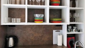 A kitchen with white shelves holding glasses, plates, and a kettle. - The stop - 4.La PSD1.7 (Zaragoza)