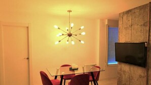 A modern dining area with a glass table, red chairs, a unique ceiling light fixture, and a mounted TV on the wall. - The stop - 4.La PSD1.7 (Zaragoza)