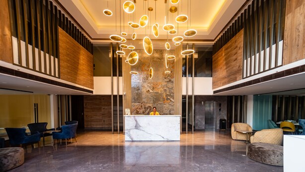 Un amplio vestíbulo con una recepción de mármol, luminarias modernas y una pared decorativa de piedra.