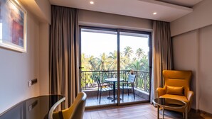 Una habitación moderna con balcón, un sillón amarillo, una mesa de vidrio y vistas a palmeras.