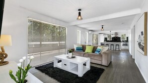 A modern living room with a sofa, coffee table, and a kitchen in the background. - Beauty AND THE Peace - Inlet Side (Inverloch)
