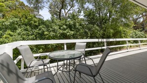 An outdoor deck with a round table and chairs, surrounded by a white railing, overlooking a lush green landscape. - Beauty AND THE Peace - Inlet Side (Inverloch)