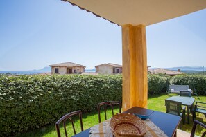 Um terraço com mesa e cadeiras, uma cesta de vime e vista para edifícios ao longe.