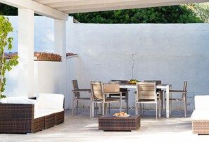 An outdoor patio with a white wall, wicker furniture, and a table set for dining. - Villetta Bianca (Olbia)
