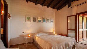 Un dormitorio con cama, una silla, una mesita de noche y una pared decorada con cuadros.