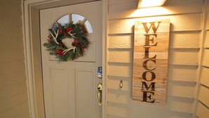 A white door with a circular window, a wreath with red berries, and a 'WELCOME' sign on the wall. - 13 Modoc-Sunriver, Oregon: Hot Tub, BBQ, WiFi, Ping Pong, Foosall, SHARC Aquatics, Tubing Hill, Mt. Bachelor, Golf, Deschutes River, Tennis, Bike Paths (Sunriver)