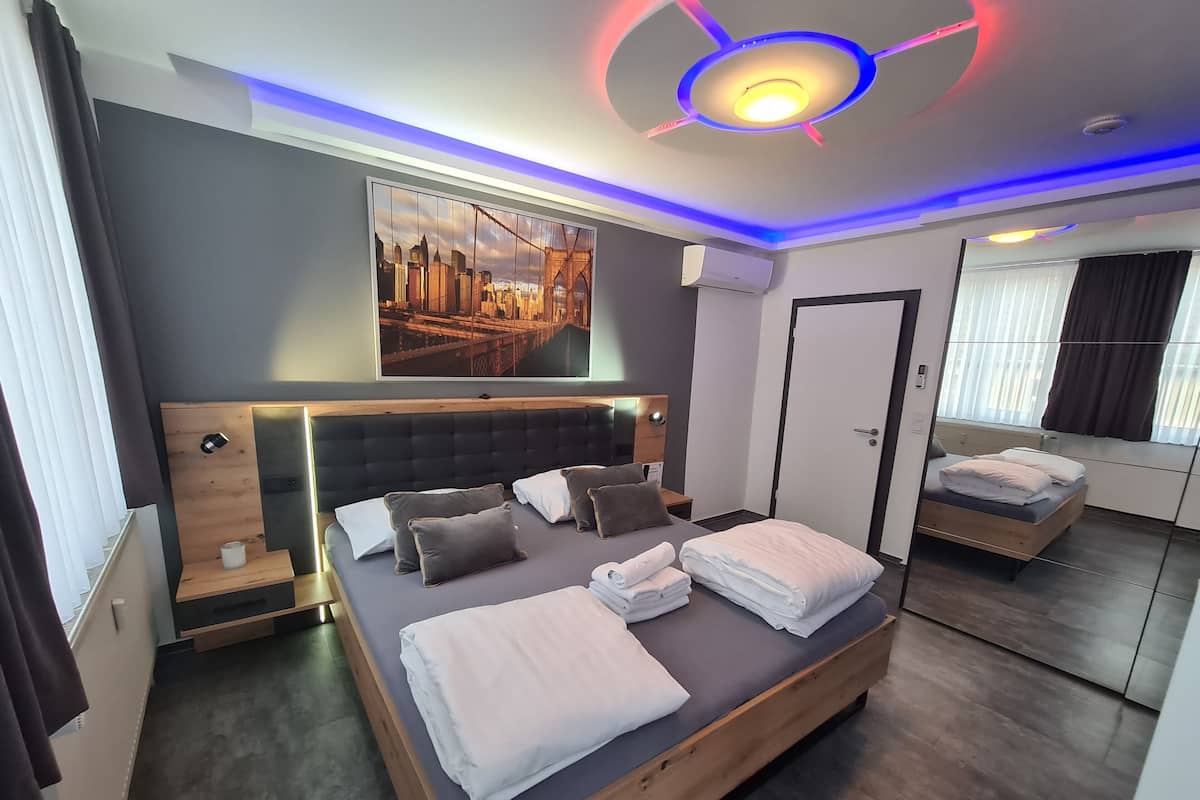 A modern hotel room with a large bed, a cityscape painting, and a unique ceiling design.