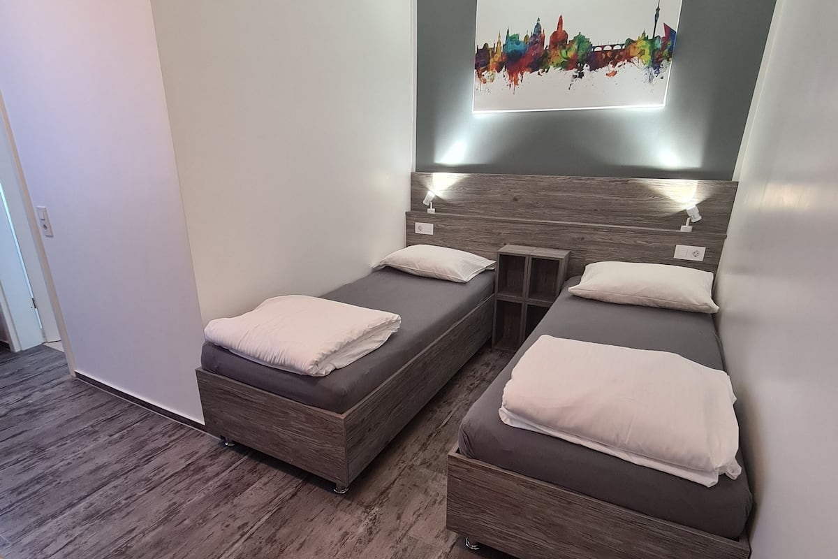 A modern bedroom with two single beds, a wooden headboard, and a colorful abstract painting on the wall.
