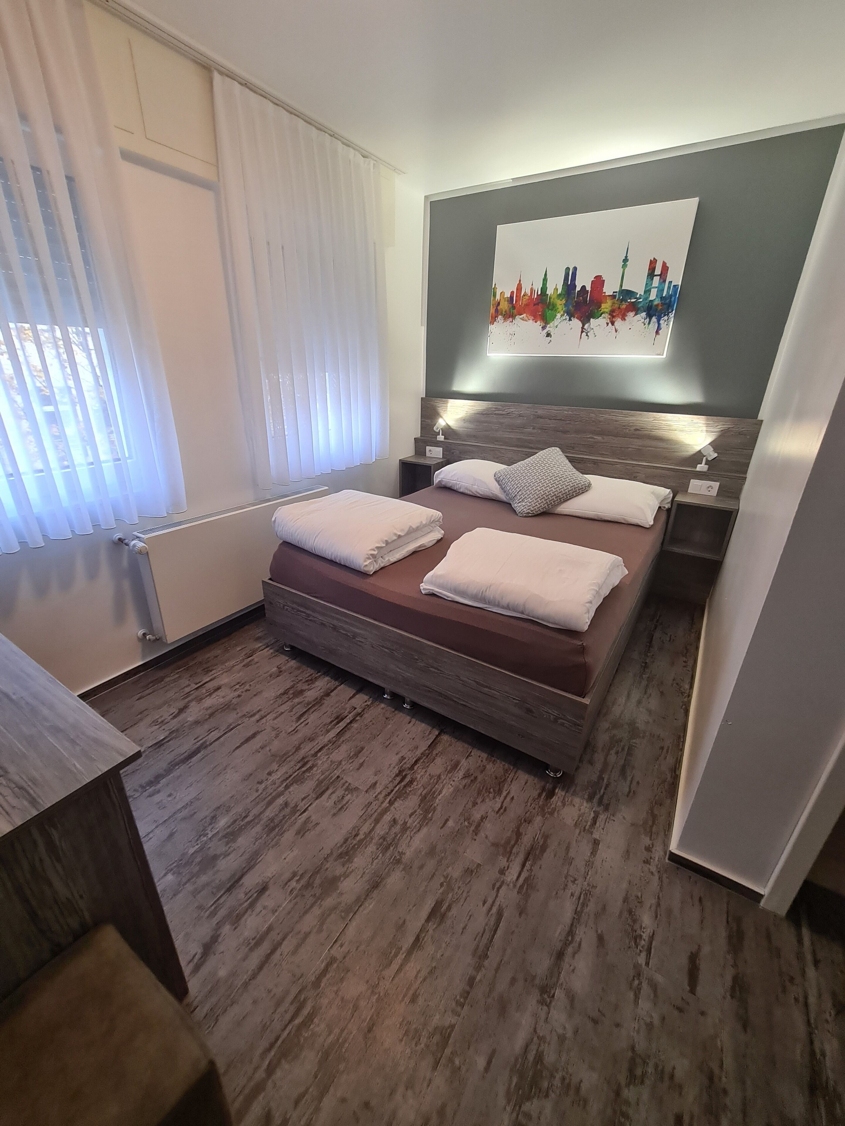A modern bedroom with a bed, bedside tables, a wall-mounted artwork, and a window with curtains.