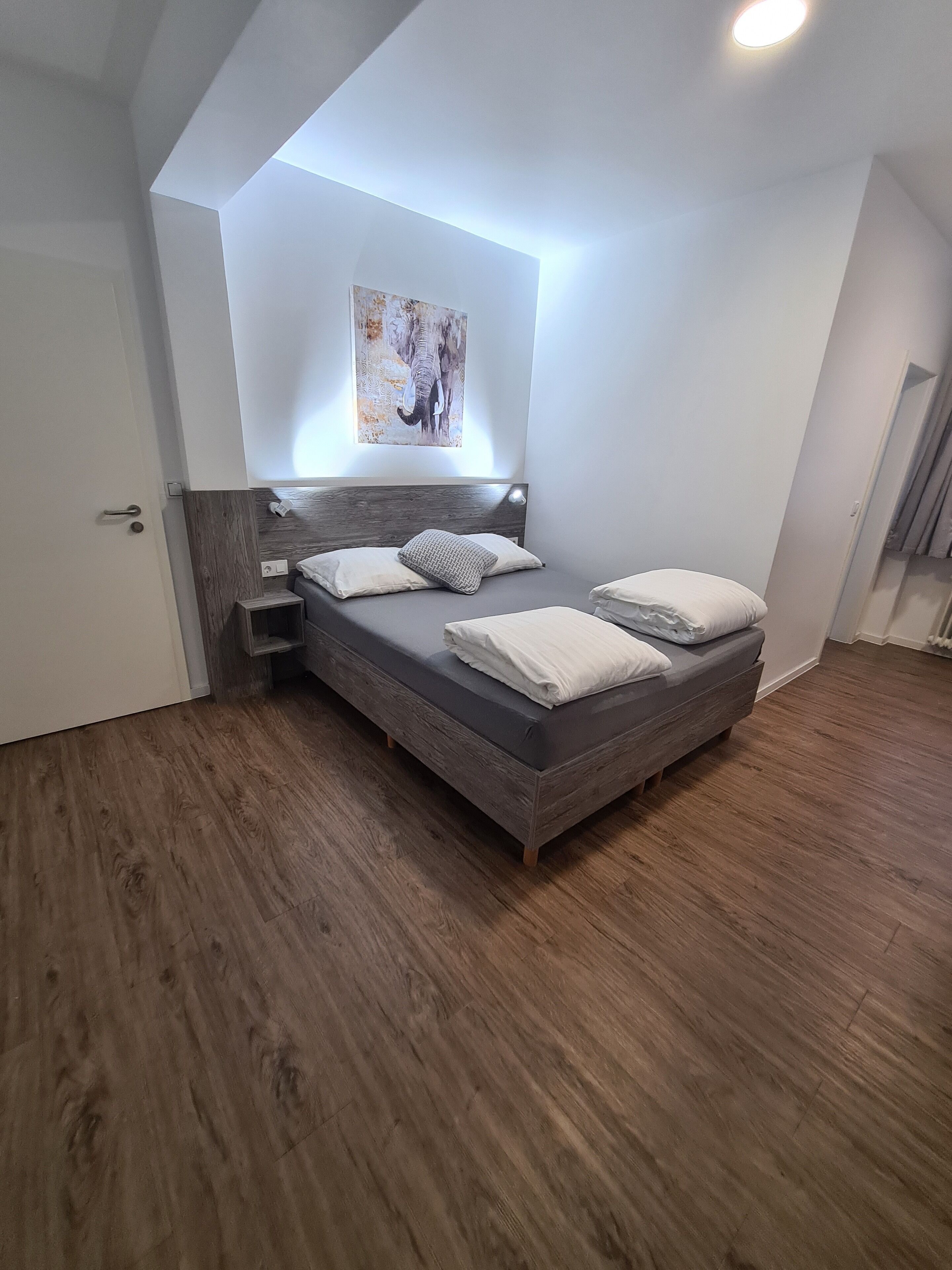 A bedroom with a bed, a headboard, a wall-mounted artwork, and a door.