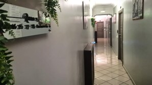 Un couloir avec un sol carrelé, un comptoir d’accueil, un panneau fixé au mur et une porte au fond.