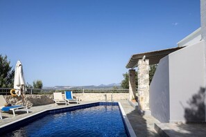 A swimming pool with a view of the landscape, a covered seating area, and a stone wall. - Sea Horizon Villa Ikaros by DomisiGroup (Ag. Triada)
