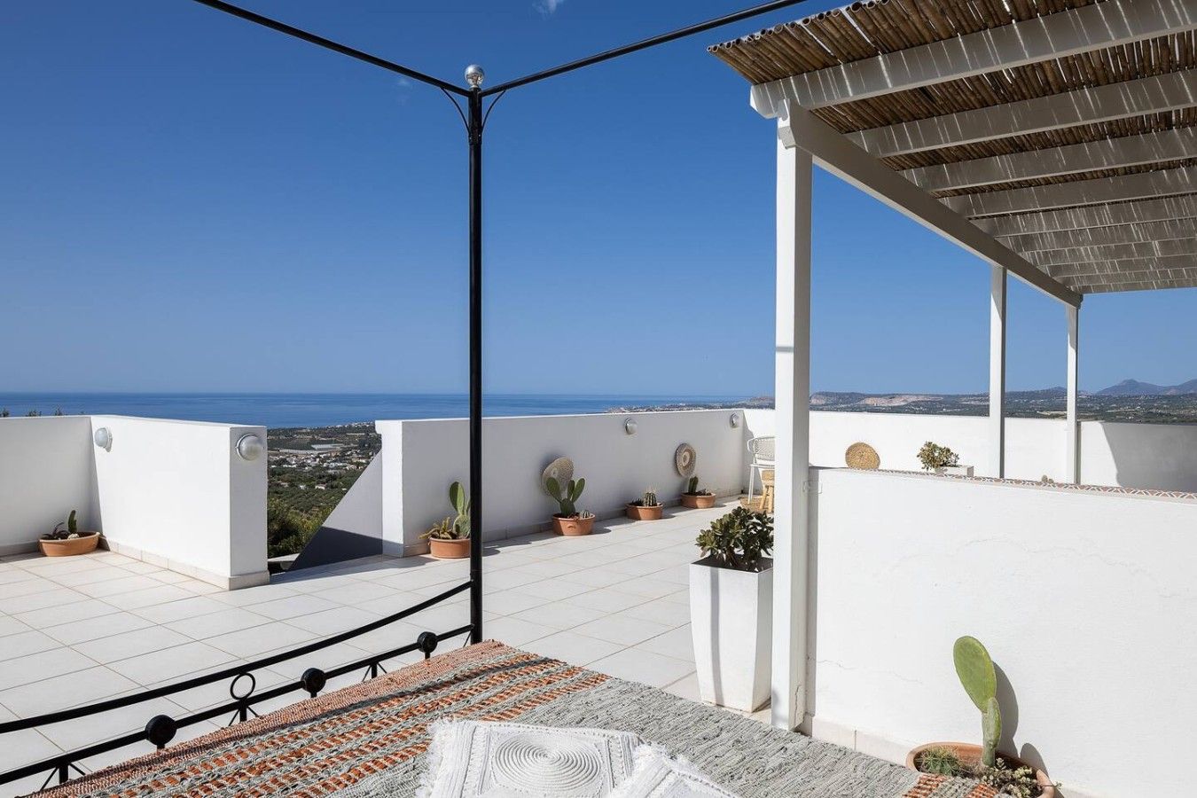 A rooftop terrace with a clear view of the sea, potted plants, and a pergola structure.