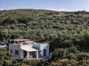 A modern two-story building with a flat roof, surrounded by dense vegetation and hills. - Sea Horizon Villa Ikaros by DomisiGroup (Ag. Triada)