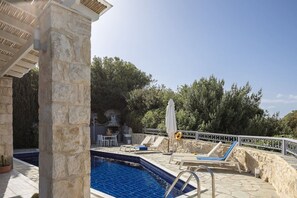An outdoor swimming pool with a stone deck, a barbecue area, and lounge chairs.