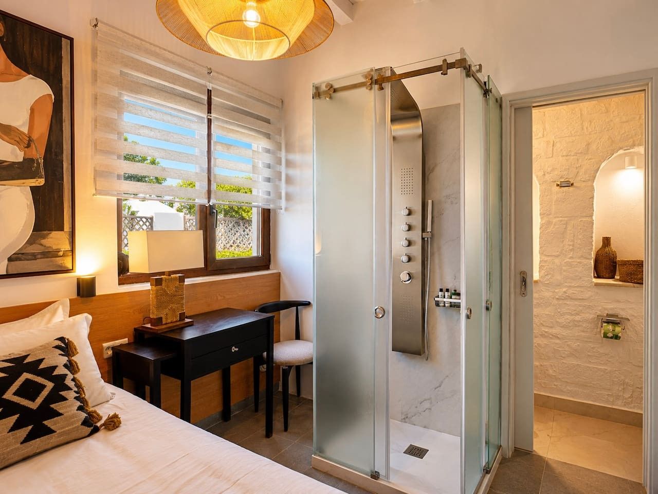 A hotel room with a bed, desk, chair, and a walk-in shower.