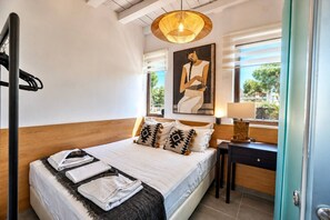 A bedroom with a bed, pillows, a bedside table, a lamp, a painting, and a window with a view. - Sea Horizon Villa Ikaros by DomisiGroup (Ag. Triada)