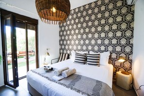 A bedroom with a large bed, a patterned wall, a wicker light fixture, and a view through a glass door. - Sea Horizon Villa Ikaros by DomisiGroup (Ag. Triada)