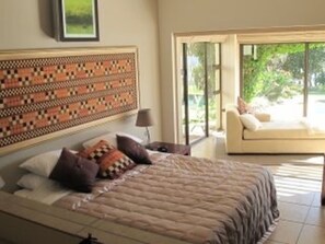 A bedroom with a bed, a nightstand, a lamp, and a view of the outdoors through a glass door.