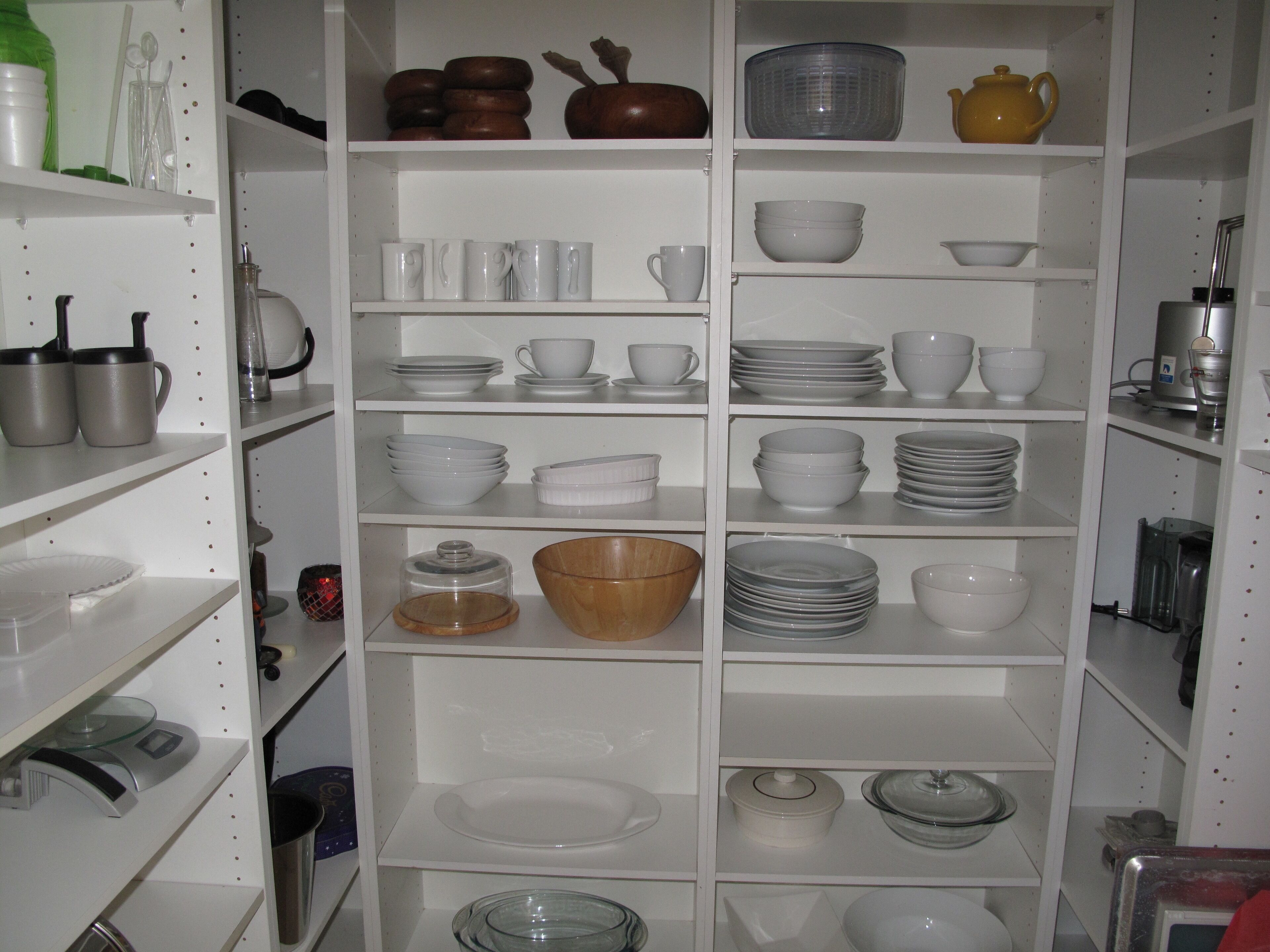 A kitchen with white shelves stocked with various dishes, bowls, and containers.