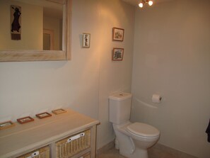 A bathroom with a toilet, a sink, and a mirror. There are three framed pictures on the wall.