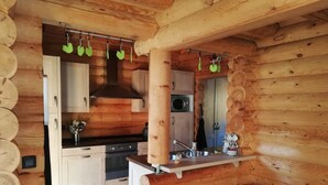 A log cabin interior with a kitchen area featuring wooden cabinets, a stove, and a hanging light fixture. - La Bresse Lodge - Air-Conditioned Log Cabin (La Bresse)