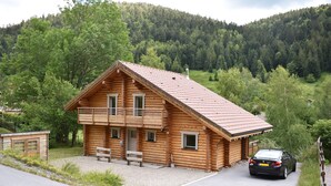 A wooden cabin with a sloped roof, a porch with benches, and a car parked in front. - La Bresse Lodge - Air-Conditioned Log Cabin (La Bresse)