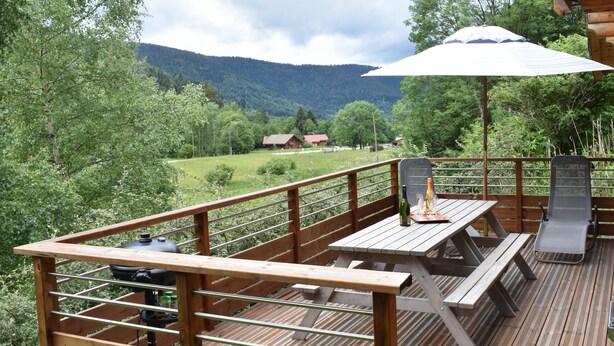 A wooden deck with picnic tables and a grill, overlooking a mountainous landscape. - La Bresse Lodge - Air-Conditioned Log Cabin (La Bresse)