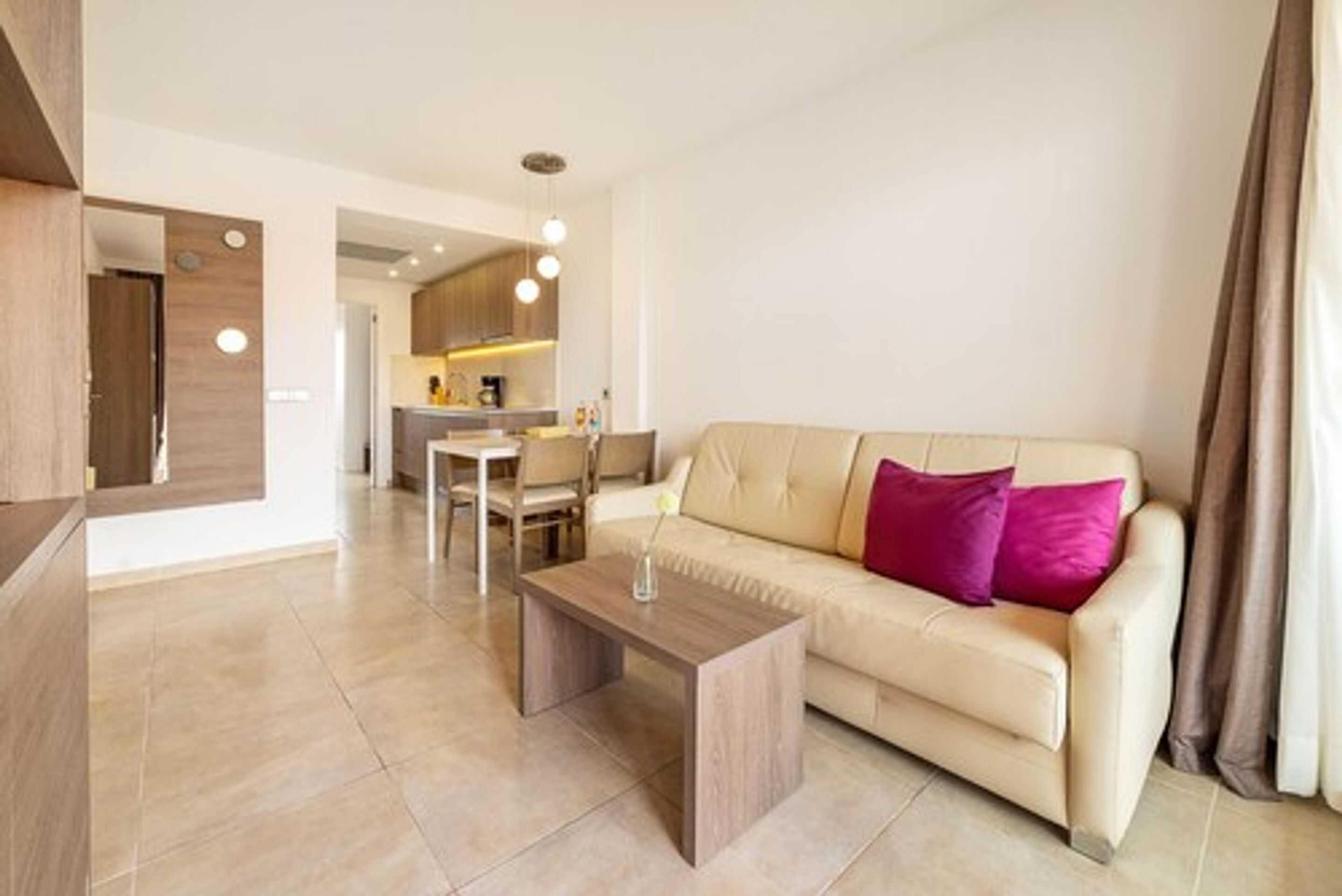 Un soggiorno moderno con un divano beige, un tavolino in legno e una cucina sullo sfondo.