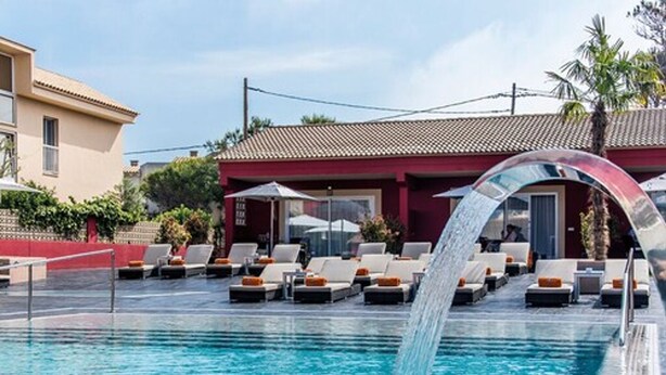 A pool with a water feature, lounge chairs, and a building with a red facade. - Hotel Paradise Residencial (Capdepera)