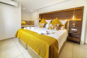 Una habitación de hotel moderna con un cabecero de madera, una cama con colcha color mostaza y una mesita de noche con lámpara.