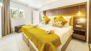 A hotel room with a large bed, a bedside table, a nightstand, a window with curtains, and a view of trees outside. - Hotel Paradise Residencial (Capdepera)