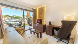 A modern living room with a sofa, a desk, a chair, a TV, and a balcony with a view of the city. - Hotel Paradise Residencial (Capdepera)