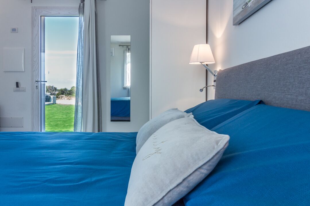 Ein Schlafzimmer mit Bett, Nachttisch, Lampe und Blick ins Freie.
