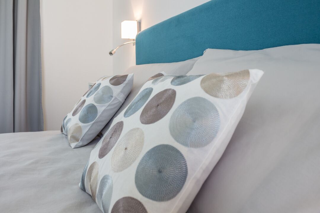 Una cama con cabecera azul y almohadas estampadas.