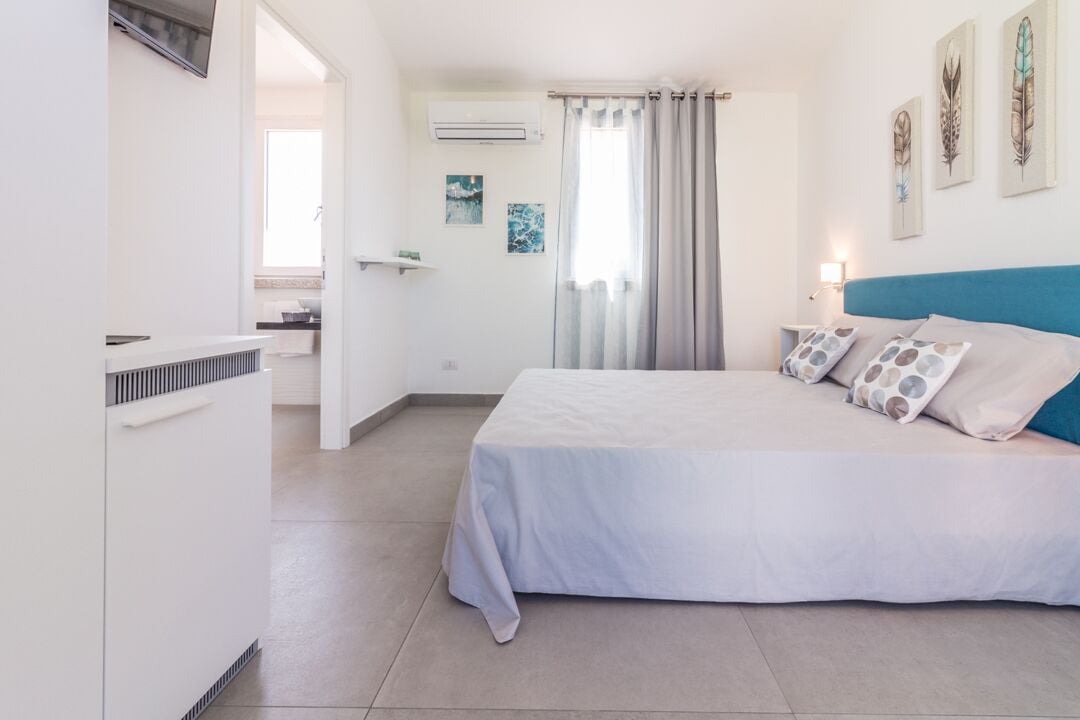 A bedroom with a bed, a TV, an air conditioner, and a window with curtains.