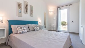 Een slaapkamer met een groot bed, een blauwgroen hoofdeinde en een schuifdeur naar een balkon.